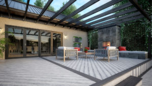 This image depicts a modern, gray wooden deck with wooden beams hanging over it and one step leading off the deck into the backyard. The deck is furnished with a coffee table surrounded by three armchairs in front of a fireplace.