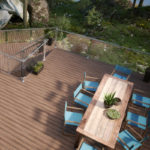A wood deck with a clear railing. The deck has a long table with eight chairs around it.