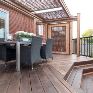 This image depicts a deck area with an outdoor dining table. There is a flower pot on the table, along with dishes and a candle.