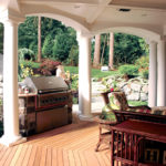 An outdoor deck featuring deck boards, a grill, outdoor furniture and white columns.