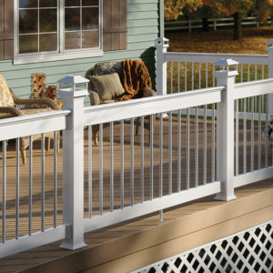 A porch with a white railing and two comfortable chairs. There is fall foliage in the background.