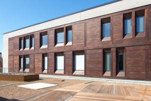 This image depicts a building with wooden cladding with various windows reflecting sunlight. 