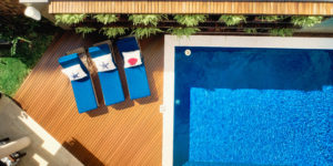 This image depicts a poolside deck area with three lounge chairs and wood deck boards.