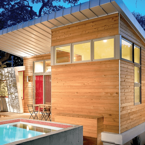 This home has wood siding with a red door. There is a pool off of the back of the home and a small eating area