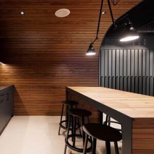 This picture depicts a kitchen with pine paneling incorporated throughout the space. There are bar stools pulled up to a counter with hanging light fixtures placed above the counter.