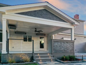 A one-story home with a porch that has a stone railing on the right and a glass railing on the left. The stairs leading up to the porch are lined with lights.