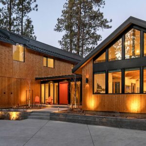 This house with wood siding has black trim. Warm lights are lit on the exterior of the home.