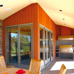 This picture depicts an outdoor area with cedar siding. There is a stainless steel grill and a seating area with a table and chairs. 