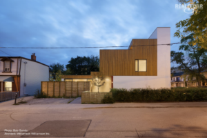 This image depicts a modern house with wood siding. The entryway lights are turned on to highlight the front of the home.