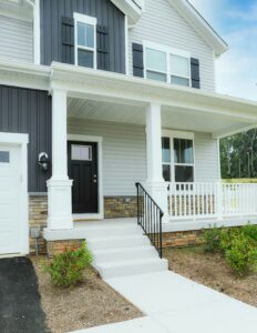 A multi-colored home has a porch with white vinyl and black metal railings. 