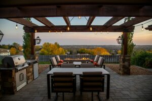 This outdoor patio features a wooden pergola, a grilling station, two sitting areas and a firepit.