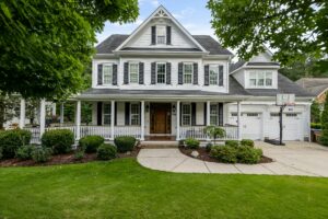 A two-story white home has a large front porch with a white railing system.