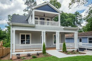 A bungalow-style home has a wood-floored porch surrounded by a white railing system.