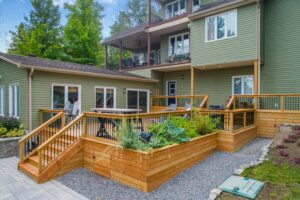 This image depicts a green house with a wooden deck. There are built-in plant boxes on the side of the deck.